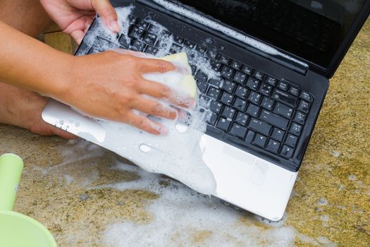 closeup cleaning computer notebook with dish washing soap, technology concept