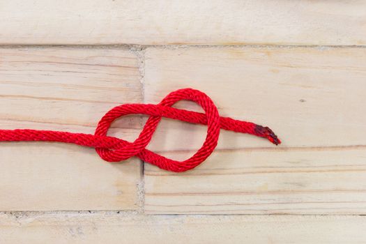 Figure-eight knot made with red rope on wooden background.