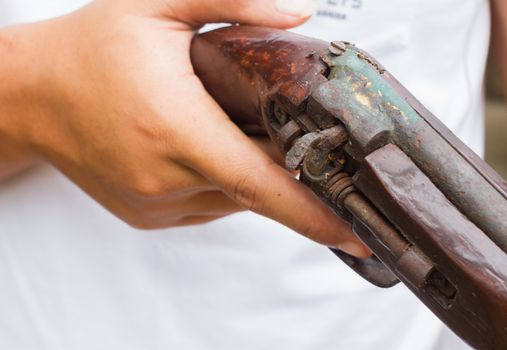 horizontal photo of closeup hand holding old gun, selective focus on the gun.