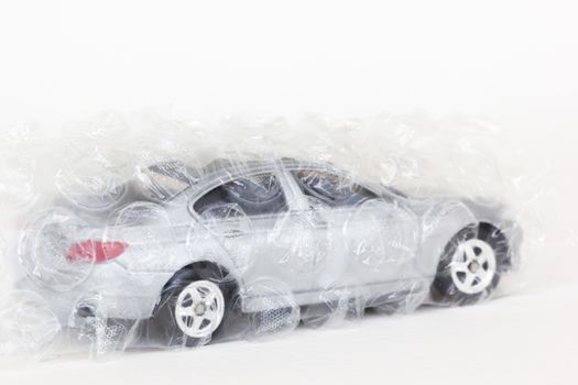 horizontal photo of a gray car toy with air bubble wrap on white background.