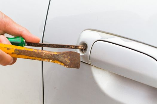 horizontal photo of closeup locksmith will open bronze car door white screwdriver - selective to focus on key hold.