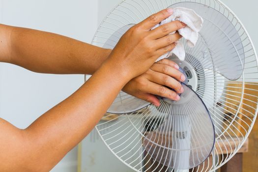 Close up horizontal photo of male hand cleaning dirty electric fan blade with cloth.