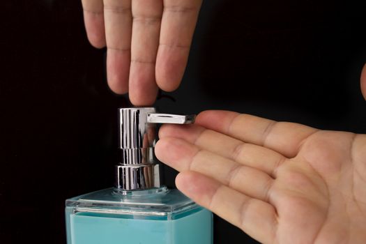 Close up of a person getting soap from a soap dispenser on a black background