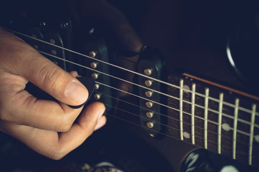 Guitarist is rehearsing playing black vintage electric guitars. Closeup  girl's hand is holding the pick and putting it on guitar string in dark studio. Concept of musical instruments and rock music.