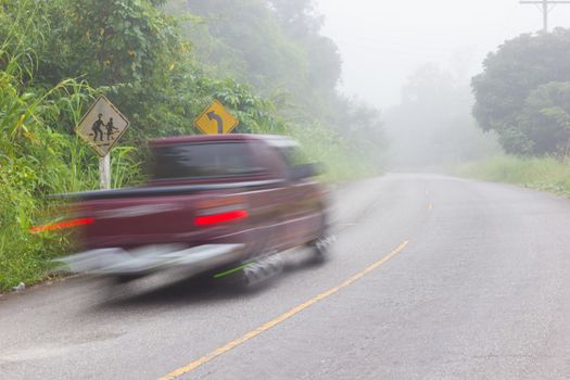 Motion blur of car on road on foggy morning along green tree lined road in the morning, Thailand.