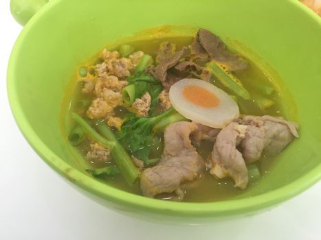 horizontal photo of noodles on green bowl with pork and vegetables on white table