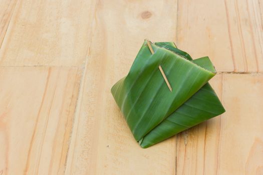 Thai food or dessert wrapped with banana leaf on wooden background. Copyspace.