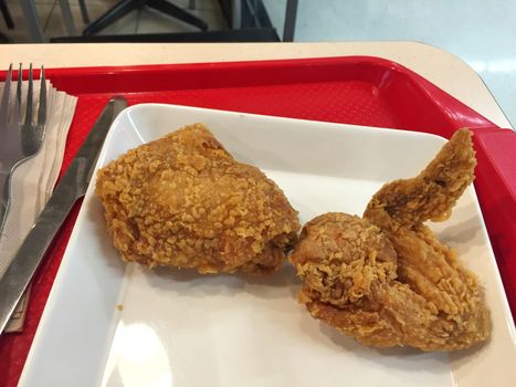 Fresh fried chicken on white dish with knife and fork in restaurant.