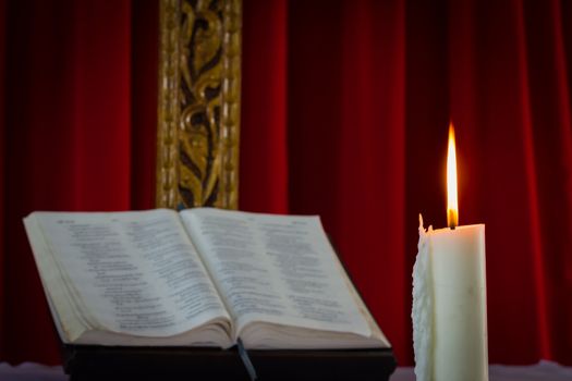 Open book and burning candle on dark