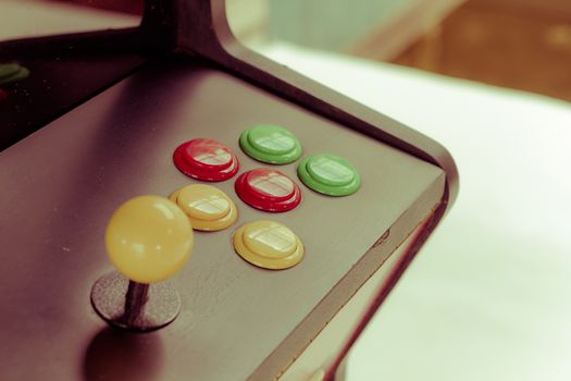 yellow joystick of an old arcade video game with six colorful button. Retro filter. Focusing on the buttons.