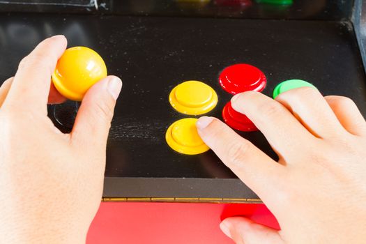 hands touching yellow joystick and buttons of old arcade video game