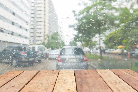 perspective wooden board empty table in front of blurred raining on the windshield of a vehicle on the street