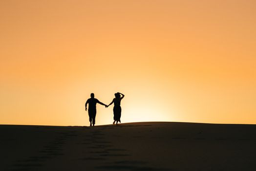 silhouettes of a happy young couple guy and girl on a background of orange sunset in the sand desert