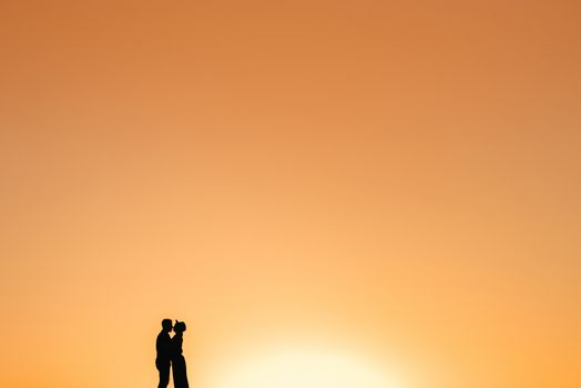 silhouettes of a happy young couple guy and girl on a background of orange sunset in the sand desert