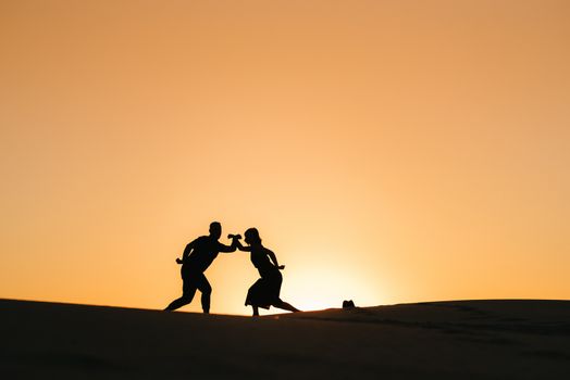 silhouettes of a happy young couple guy and girl on a background of orange sunset in the sand desert