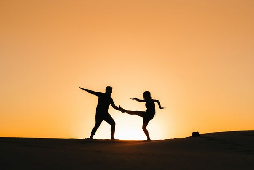 silhouettes of a happy young couple guy and girl on a background of orange sunset in the sand desert