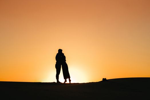 silhouettes of a happy young couple guy and girl on a background of orange sunset in the sand desert