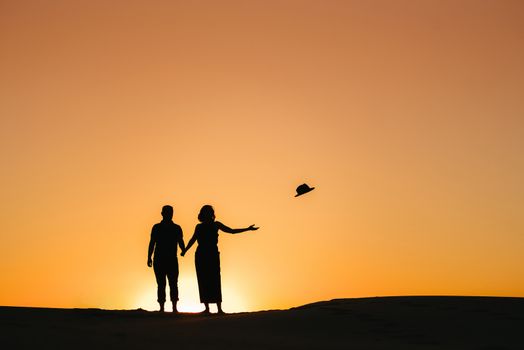 silhouettes of a happy young couple guy and girl on a background of orange sunset in the sand desert