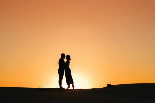 silhouettes of a happy young couple guy and girl on a background of orange sunset in the sand desert