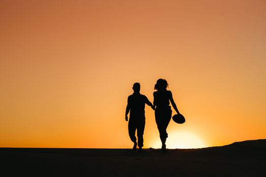 silhouettes of a happy young couple guy and girl on a background of orange sunset in the sand desert