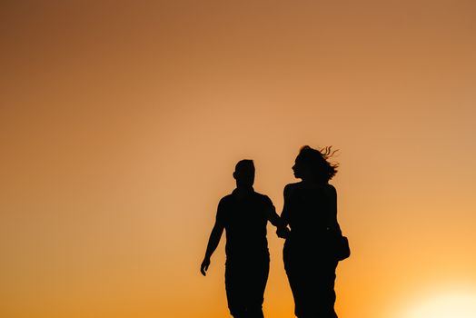 silhouettes of a happy young couple guy and girl on a background of orange sunset in the sand desert