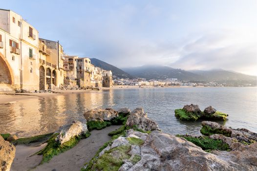 Idyllic view of houses and long sandy beach seen from the old harbour on a sunny day in Cefalu, Sicily, Southern Italy.