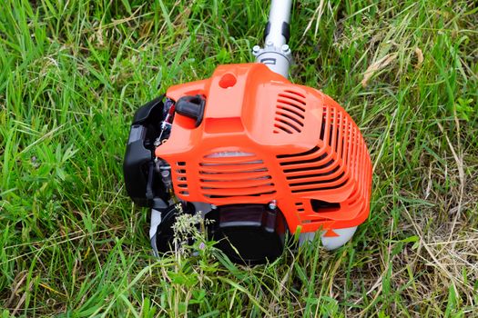 The engine of a gas trimmer lies on the grass. Power part of the trimmer. Trimer gascosis with a leaf for mowing grass and shrubs.