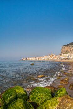 Idyllic view of Cefalu from the long sandy beach. Cathedral and Rocca di Cefalu rocky mountain on a sunny day in Cefalu, Sicily, Southern Italy.