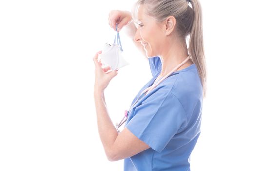 Doctor, nurse or other healthcare worker putting on a respirator N95 face mask.  She is wearing blue scrubs and a stethoscope hangs around her neck. COVID-19 coronavirus or influenza pandemic or other infectios disease