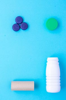 Recycling garbage. White plastic bottle, green cap, blue caps, finished paper roll arranged in a square shape on a blue background