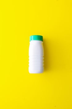 White plastic bottle with a green cap on a yellow background located in the center. Recycling plastic to the yellow container