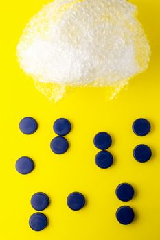 Conceptual photo of plastic bubbles representing a cloud and blue bottle caps representing rain water on a yellow background. Recycling plastic to the yellow container