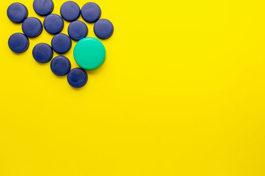 Plastic bottle caps located in the upper left corner on a yellow background. Recycling concept to the yellow container.