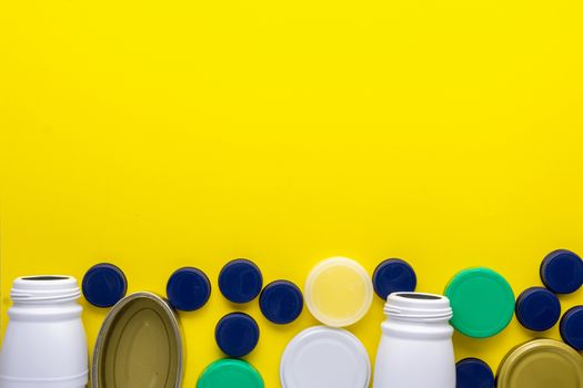 Plastic bottle caps, empty can and white plastic bottle lying down on a yellow background. Garbage and recycling concept to the yellow container.