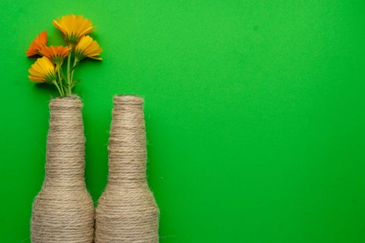 Two glass bottles of beer reused with hemp yarn and flowers on the left with a green background. Recycling and reusable concept