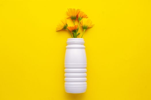 White plastic reused bottle with flowers on a yellow background located in the center. Recycling plastic to the yellow container