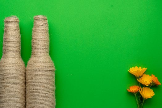 Two glass bottles of beer reused with hemp yarn and flowers on the left with a green background. Recycling and reusable concept