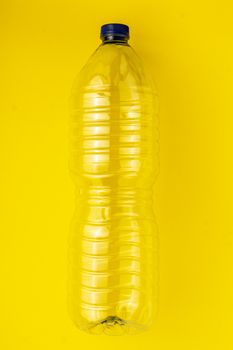 Empty plastic bottle of water on a yellow background. Concept of collecting garbage to the yellow container