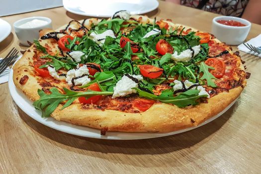 Lunch at a restaurant with friends - a big pizza with rucola tomatoes and mozzarella on the table in close-up