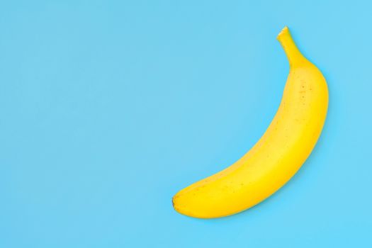 Funny concept image - single banana isolated on a trendy turquoise background in top view with copy space.