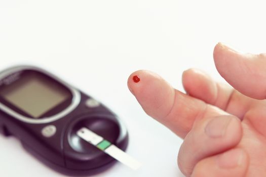 Diabetes health care concept - close up of senior man hands checking blood sugar level by glucometer.