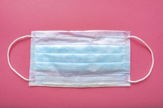 A medical surgical face mask on a pink background