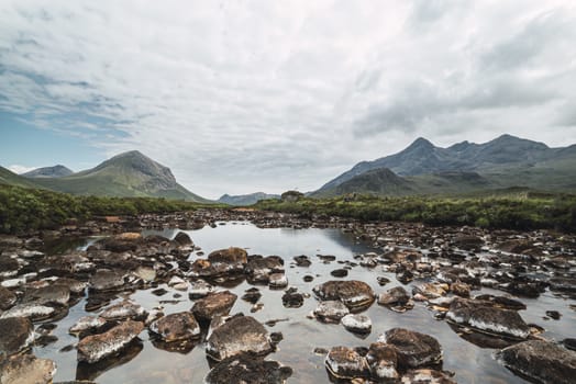 Beautiful landscape of a river with rocks and mountains in Scotland in a cloudy day