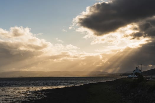 Sunset in the ocean with clouds and sun beams with an old house in the background