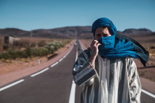 Arab person with blue bereber turban in middle of a road near desert