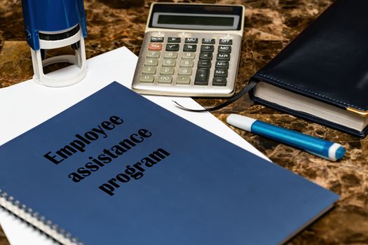 The EAP employee assistance program is written on a blue book lying on a marble Desk in the office among papers