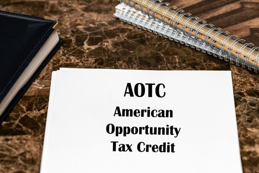 Financial concept about American Opportunity Tax Credit AOTC with phrase on the page. The text is written on a white sheet that lies on the office marble table.