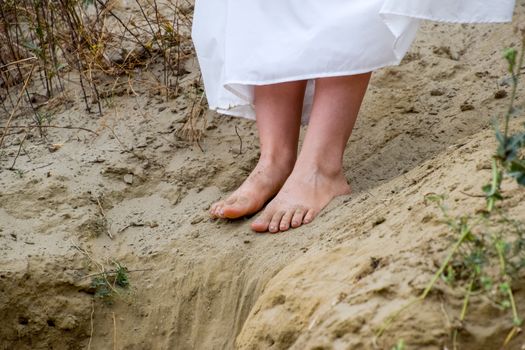 Legs of a girl in a white dress on the edge of a cliff. The sand is falling from the edge of the cliff.