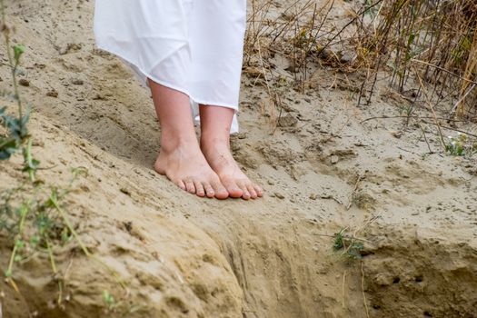 Legs of a girl in a white dress on the edge of a cliff. The sand is falling from the edge of the cliff.