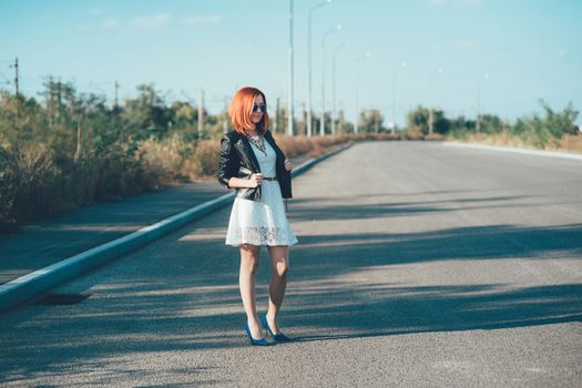 red-haired girl in a black jacket and blue glasses on a gray road